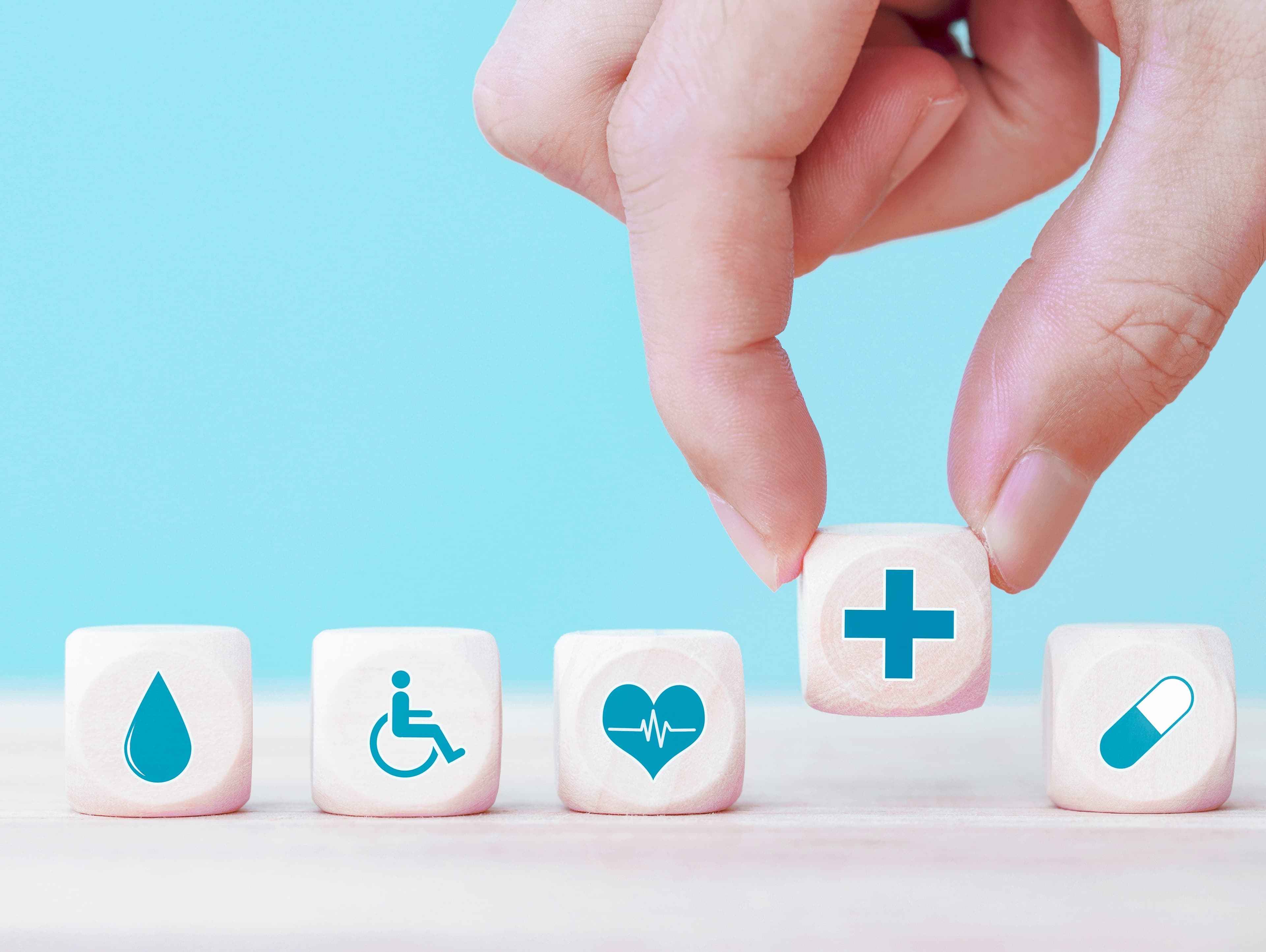 Fünf Würfel mit medizinischen Symbolen. Würfel mit + wird von zwei Fingern hochgehoben.