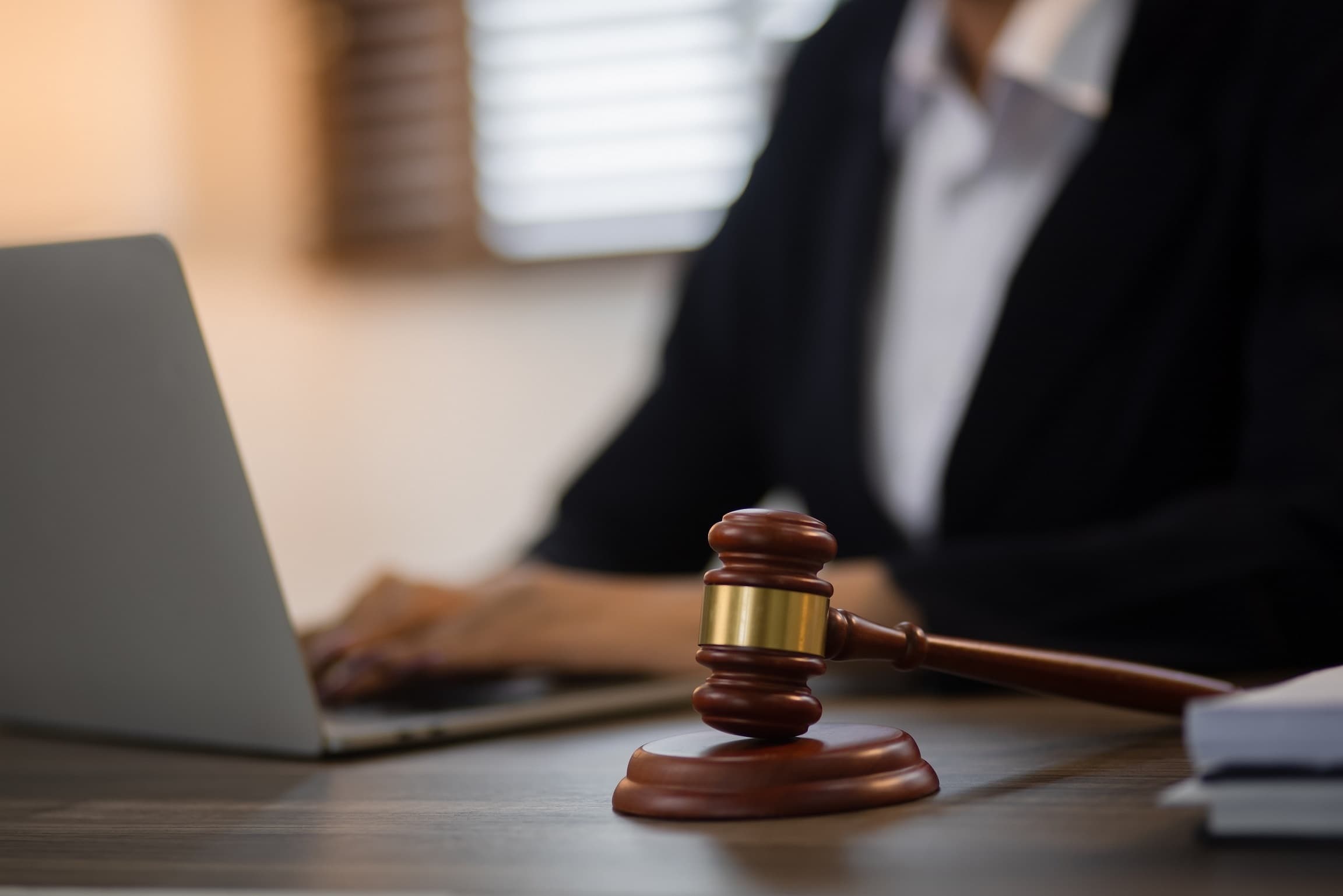 Frau an Laptop. Im Vordergrund steht ein Richterhammer.