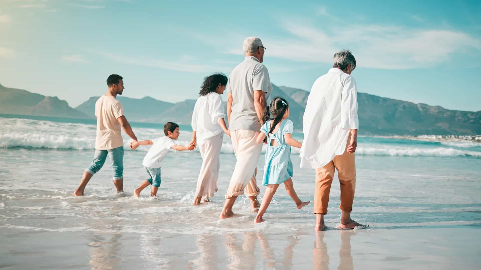 Familie mit 6 Personen geht Hand in Hand am Meer spazieren.